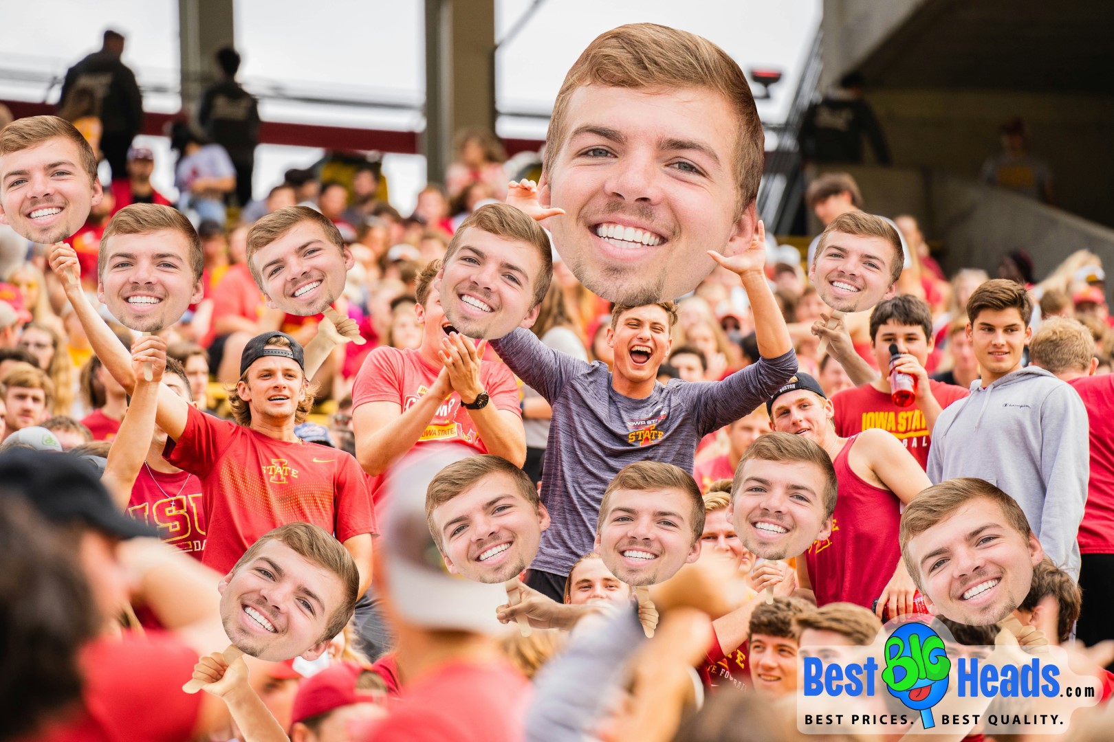 A crowd of enthusiastic fans at a sports event is cheering and holding up large, identical big head cutouts of a smiling man. The group is dressed in red and yellow, indicating team spirit, with the logo of "Best BIG Heads™" visible at the bottom right corner. The big head cutouts dominate the scene, adding a fun and lively atmosphere to the event.